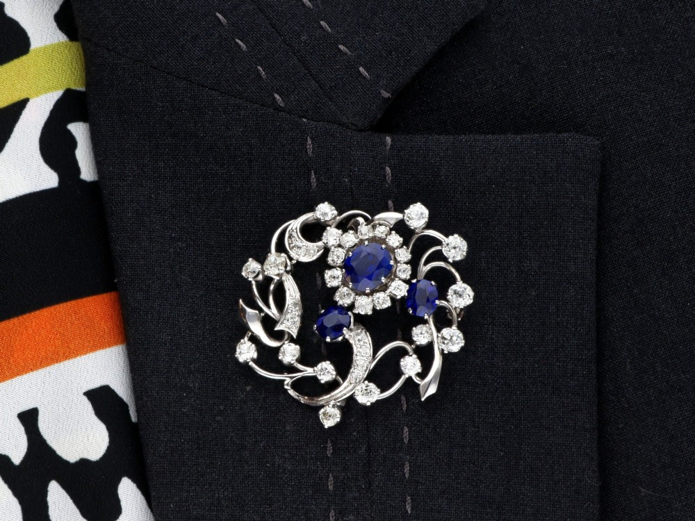 An Edwardian 18ct white gold brooch set with three oval blue sapphires surrounded by openwork diamond-set scrollwork. View X