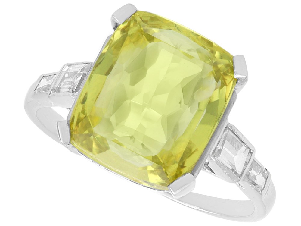 An Art Deco platinum ring featuring a large cushion cut yellow chrysoberyl central gemstone flanked by step cut diamonds on the shoulders.
