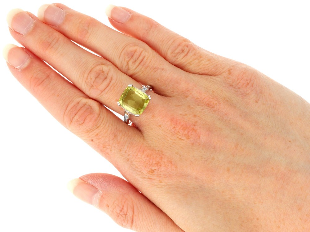 An Art Deco platinum ring featuring a large cushion cut yellow chrysoberyl central gemstone flanked by step cut diamonds on the shoulders. View IX