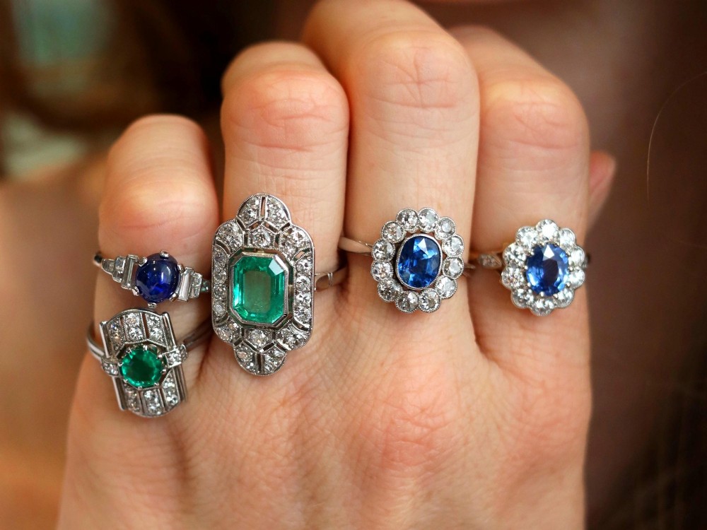 An antique platinum cluster ring featuring a central oval blue sapphire framed by twelve round cut diamonds with millegrain detail. View V