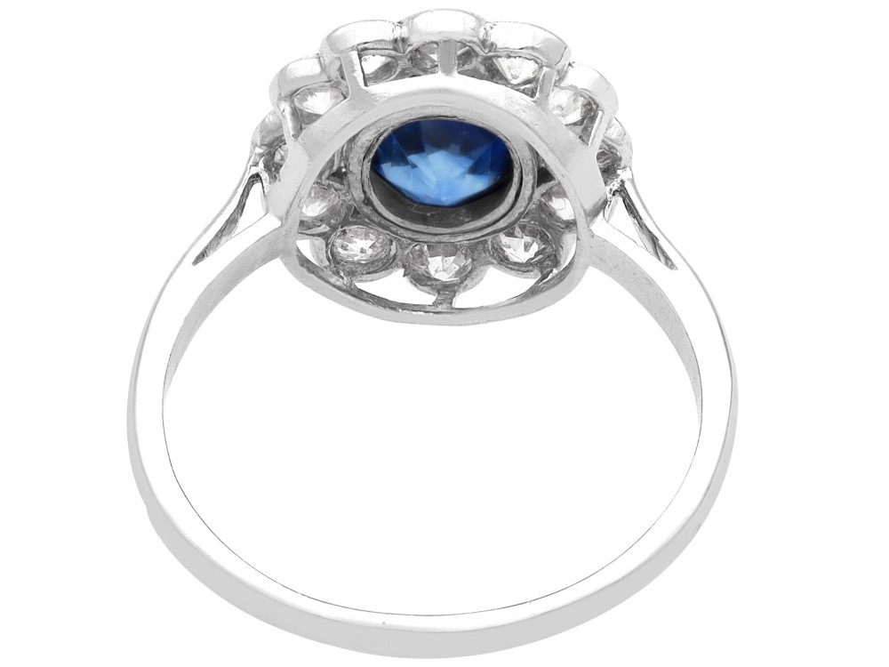 An antique platinum cluster ring featuring a central oval blue sapphire framed by twelve round cut diamonds with millegrain detail. View VII