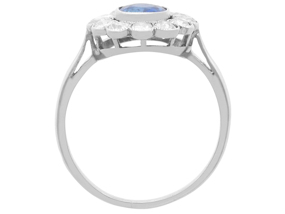 An antique platinum cluster ring featuring a central oval blue sapphire framed by twelve round cut diamonds with millegrain detail. View VIII