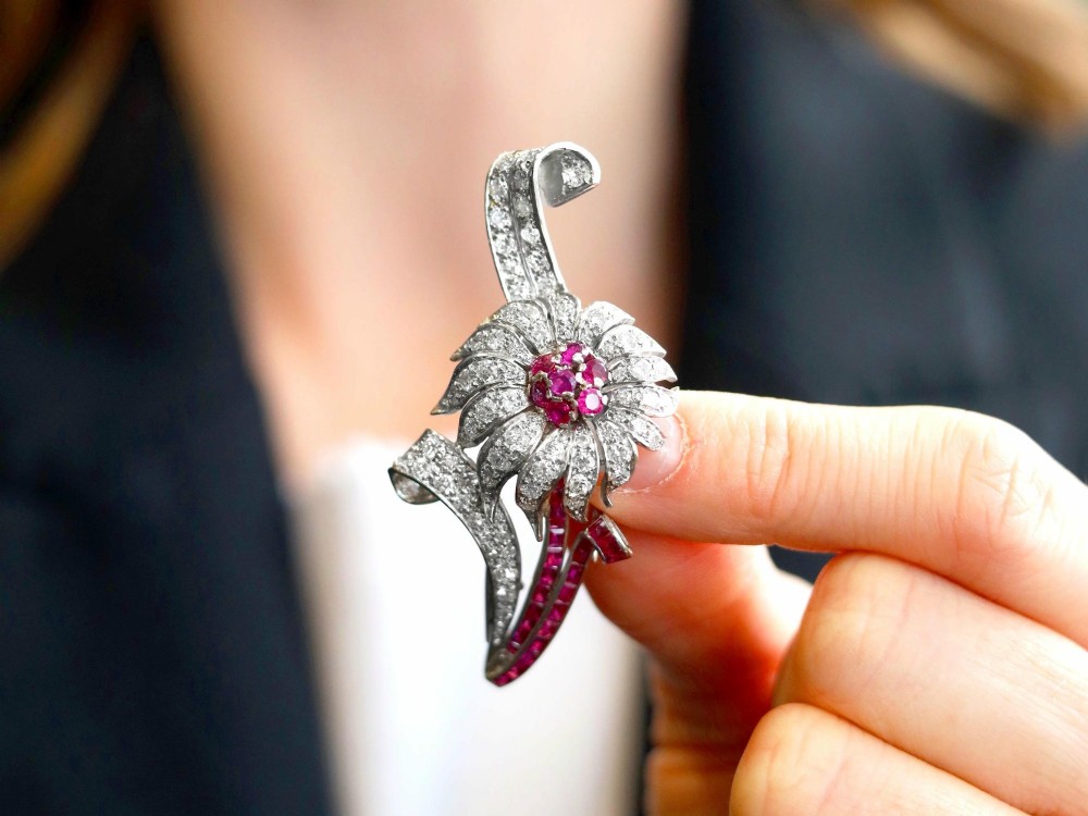 A platinum flower brooch featuring diamond-set petals, a cluster of rubies at the centre, and a stem lined with channel-set red rubies. View III