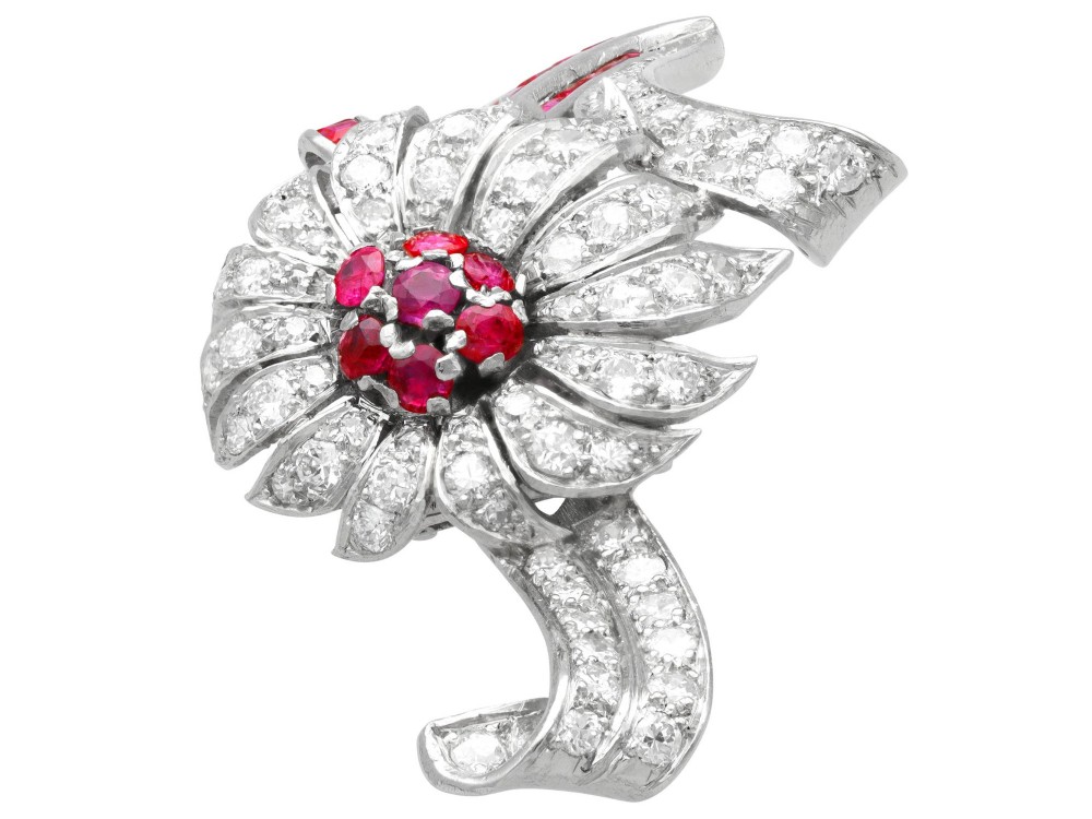 A platinum flower brooch featuring diamond-set petals, a cluster of rubies at the centre, and a stem lined with channel-set red rubies. View VI