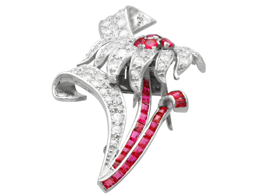 A platinum flower brooch featuring diamond-set petals, a cluster of rubies at the centre, and a stem lined with channel-set red rubies. View VII