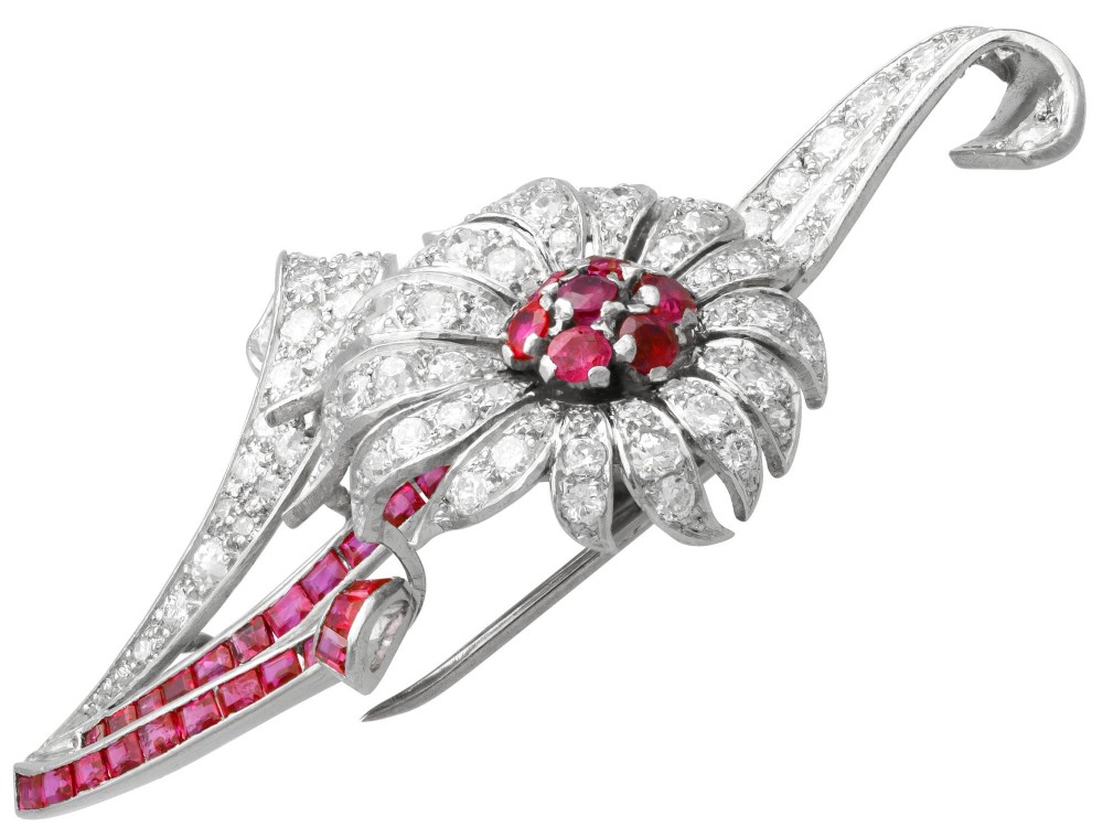 A platinum flower brooch featuring diamond-set petals, a cluster of rubies at the centre, and a stem lined with channel-set red rubies. View VIII