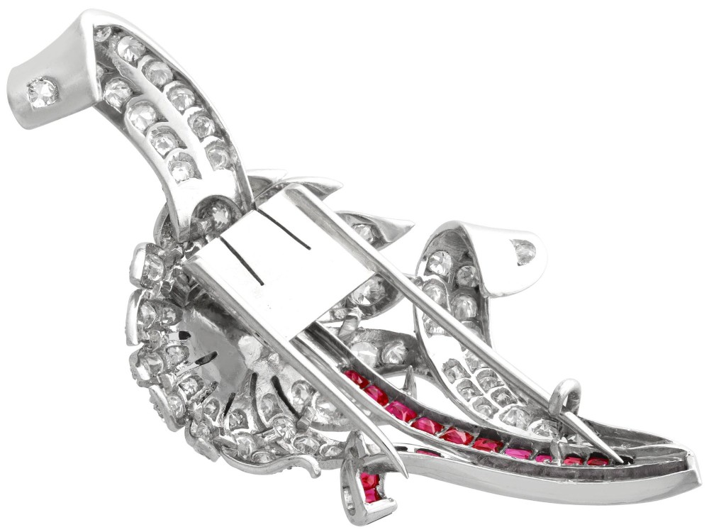 A platinum flower brooch featuring diamond-set petals, a cluster of rubies at the centre, and a stem lined with channel-set red rubies. View IX