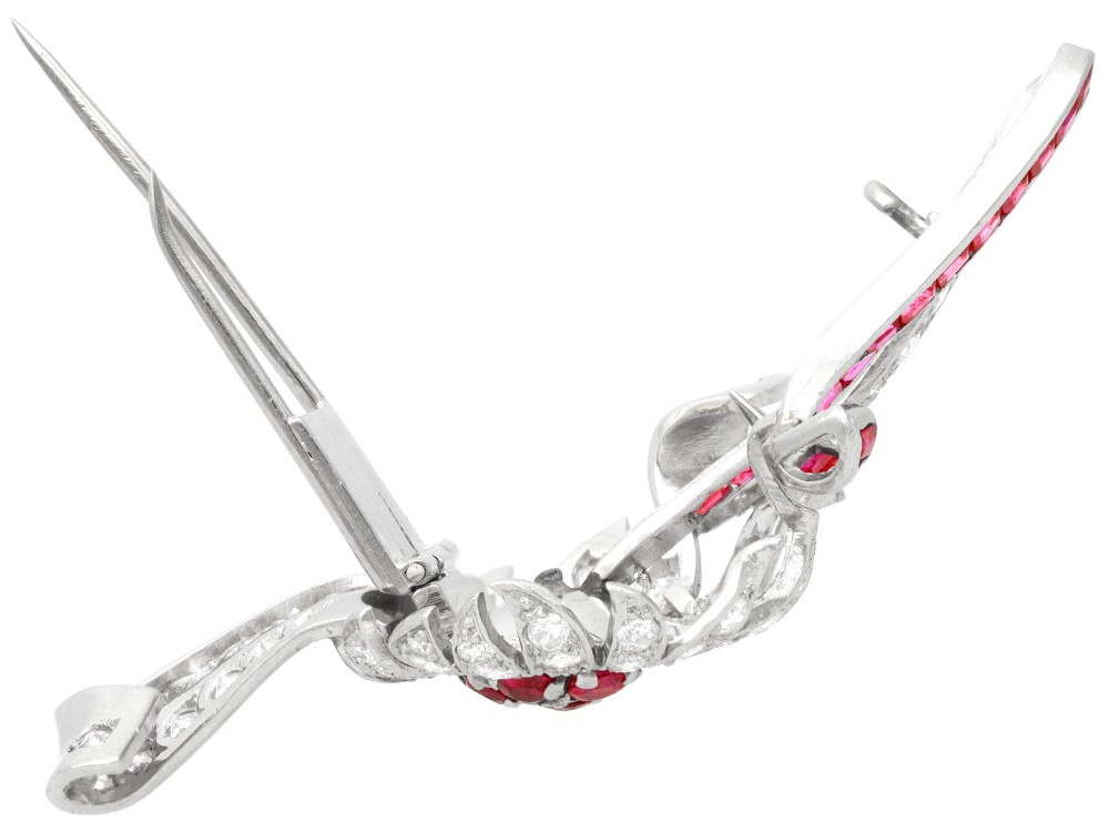 A platinum flower brooch featuring diamond-set petals, a cluster of rubies at the centre, and a stem lined with channel-set red rubies. View X
