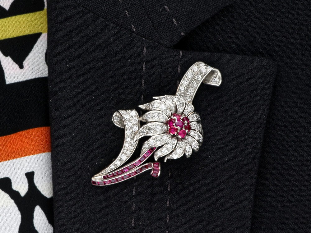 A platinum flower brooch featuring diamond-set petals, a cluster of rubies at the centre, and a stem lined with channel-set red rubies. View XIII