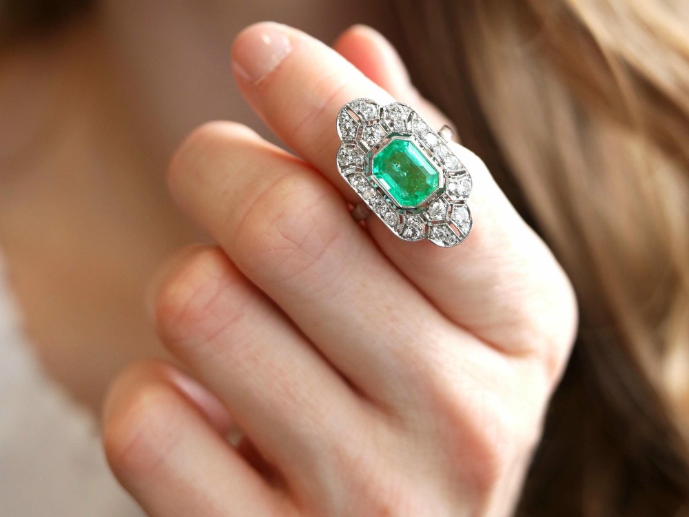 An Art Deco platinum dress ring featuring a central rectangular emerald surrounded by an elongated geometric pierced frame set with diamonds. View VI