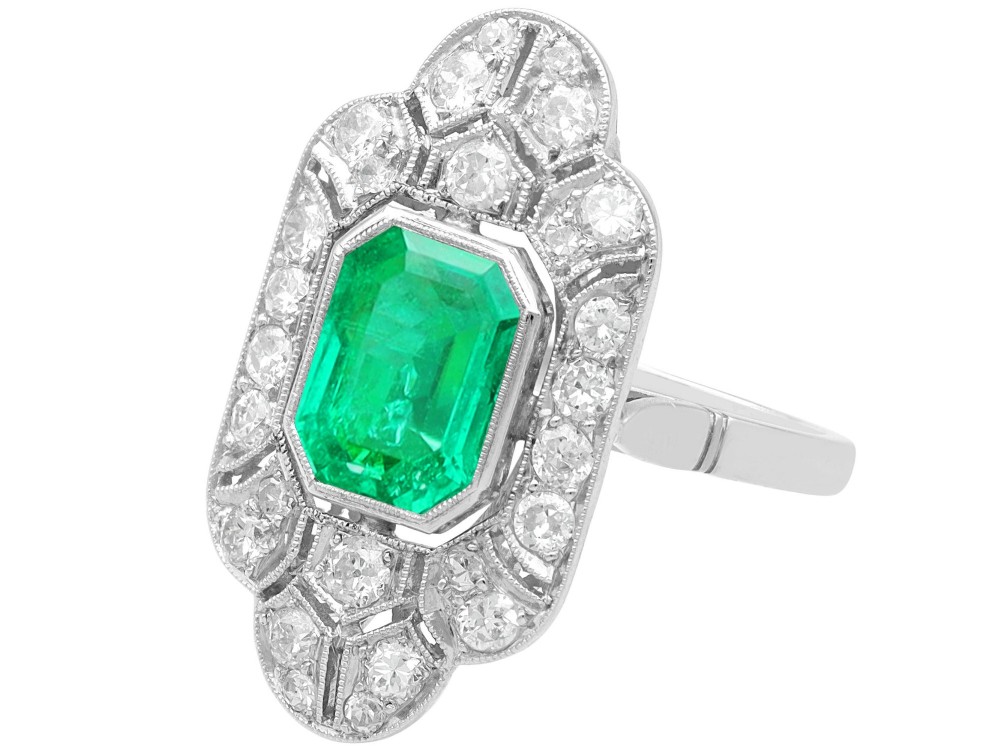 An Art Deco platinum dress ring featuring a central rectangular emerald surrounded by an elongated geometric pierced frame set with diamonds. View VII
