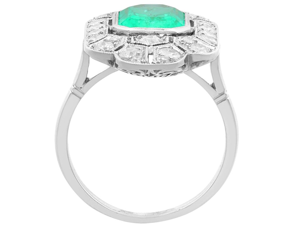 An Art Deco platinum dress ring featuring a central rectangular emerald surrounded by an elongated geometric pierced frame set with diamonds. View IX