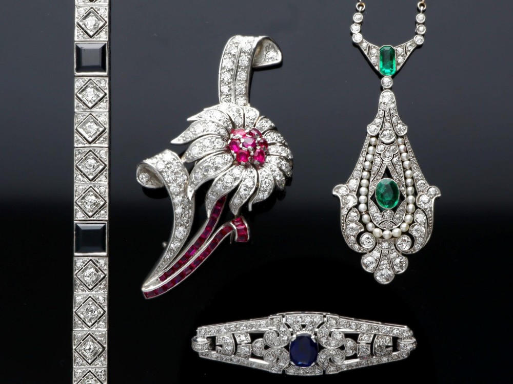 An openwork platinum pendant featuring an elongated drop shape set with diamonds, a line of seed pearls, and two vibrant green Colombian emeralds. View VII