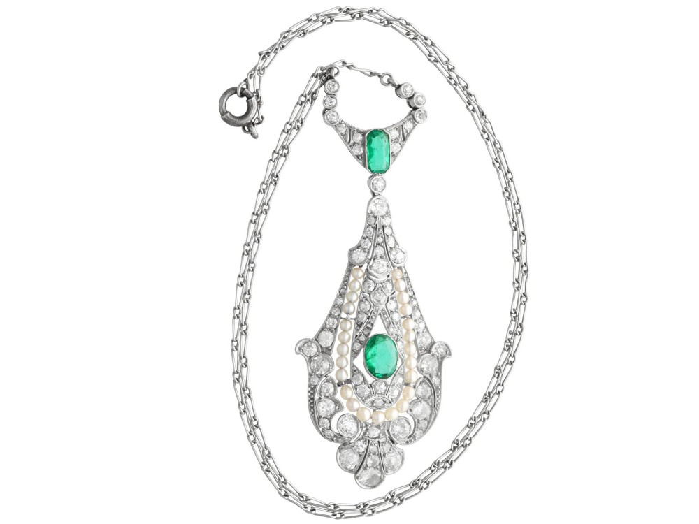 An openwork platinum pendant featuring an elongated drop shape set with diamonds, a line of seed pearls, and two vibrant green Colombian emeralds. View VIII