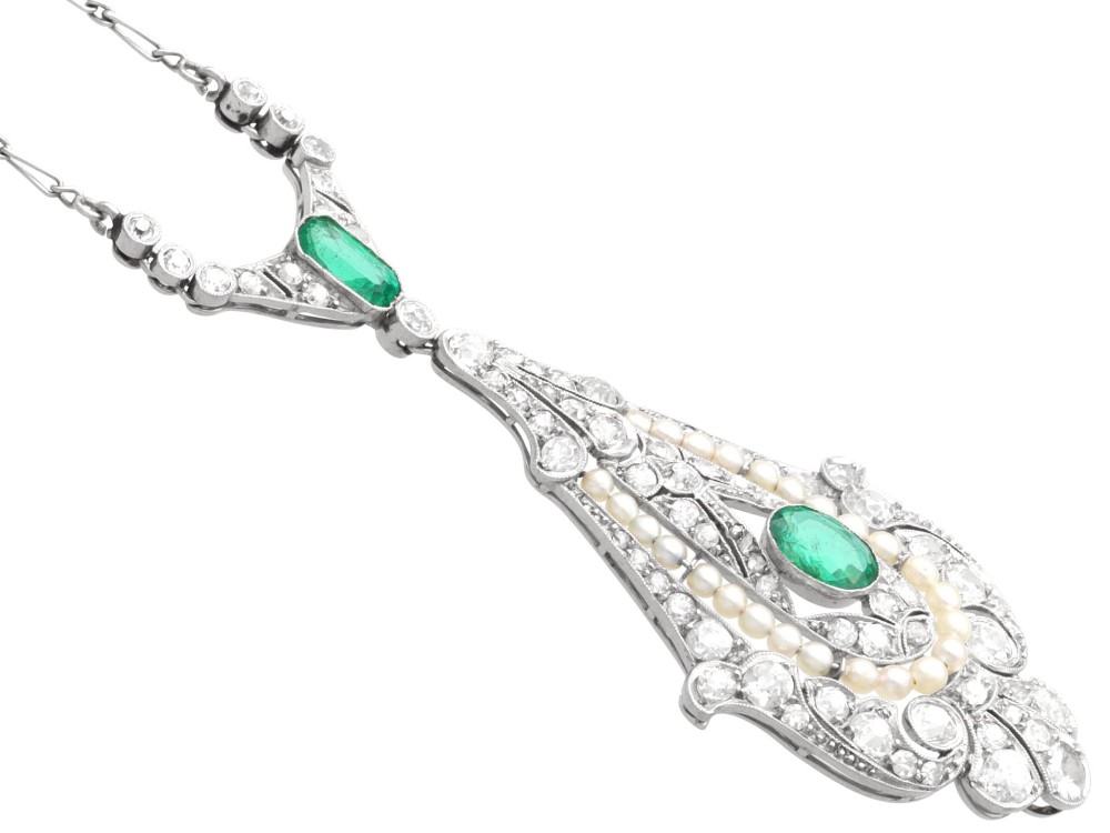 An openwork platinum pendant featuring an elongated drop shape set with diamonds, a line of seed pearls, and two vibrant green Colombian emeralds. View IX