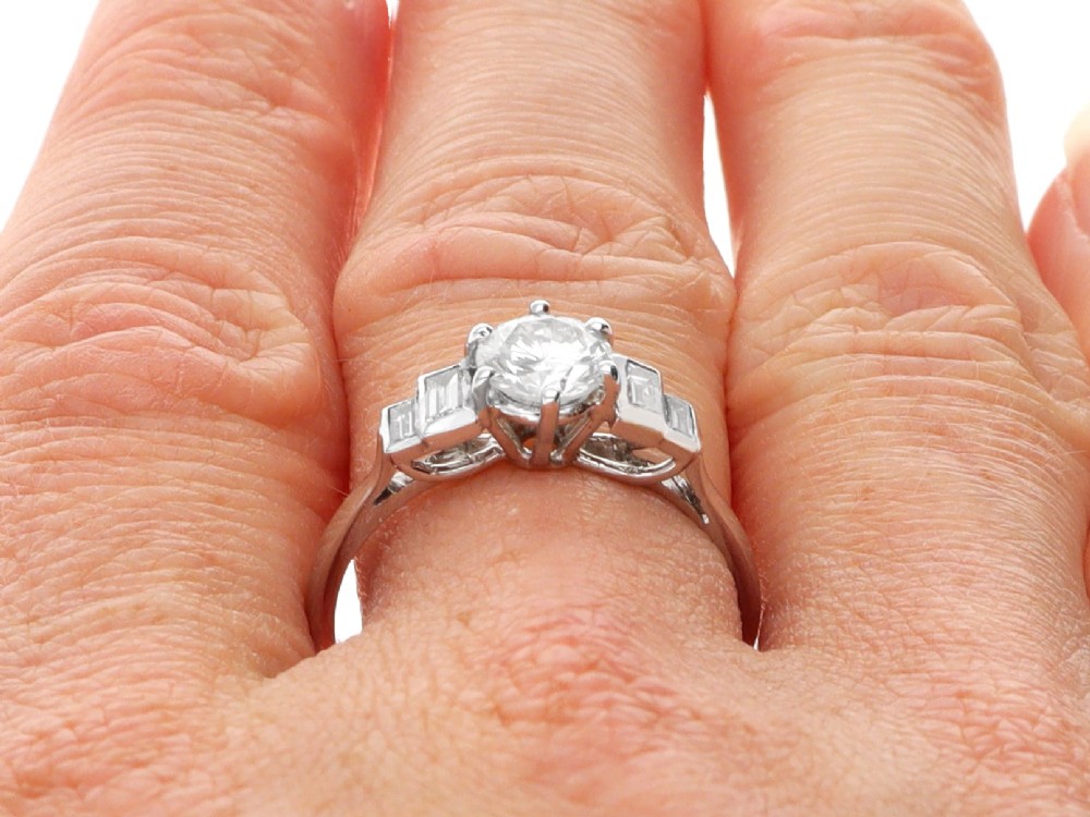 An 18ct white gold Art Deco ring featuring a central round diamond flanked by stepped baguette diamond shoulders. View IX