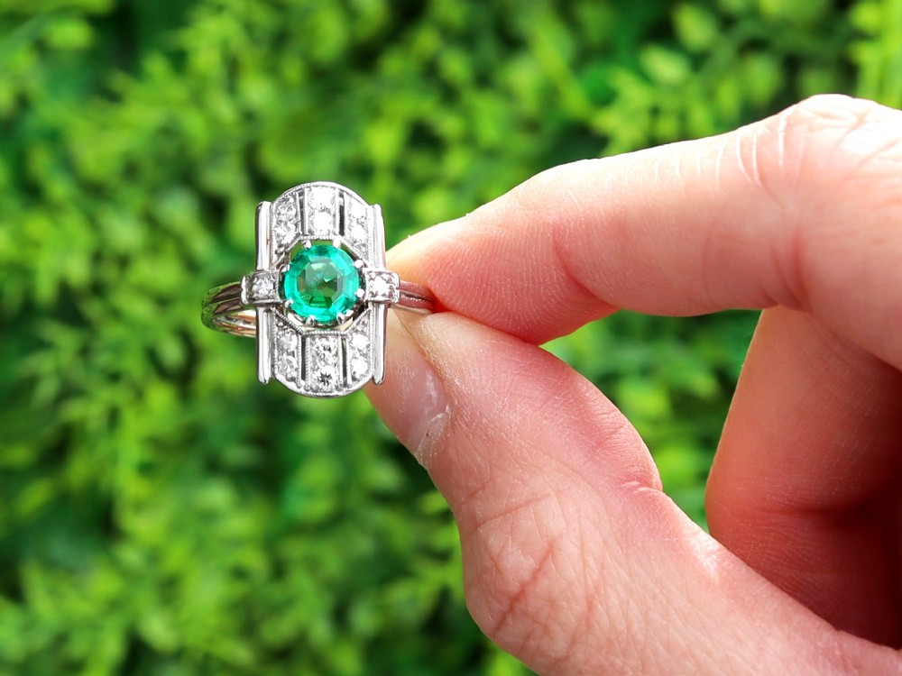 An Art Deco 14ct white gold ring featuring a central round green emerald framed by geometric shoulders set with small brilliant diamonds. View II