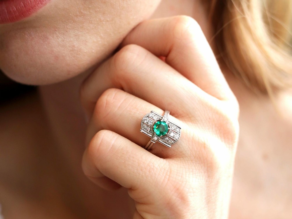 An Art Deco 14ct white gold ring featuring a central round green emerald framed by geometric shoulders set with small brilliant diamonds. View III