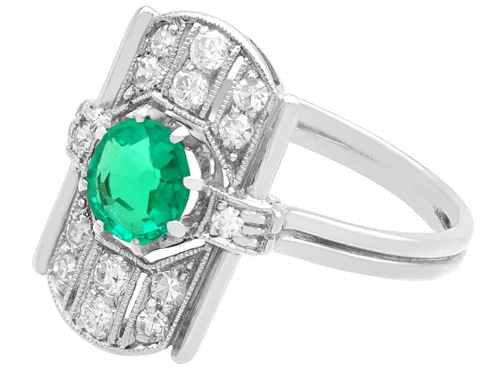 An Art Deco 14ct white gold ring featuring a central round green emerald framed by geometric shoulders set with small brilliant diamonds. View IV