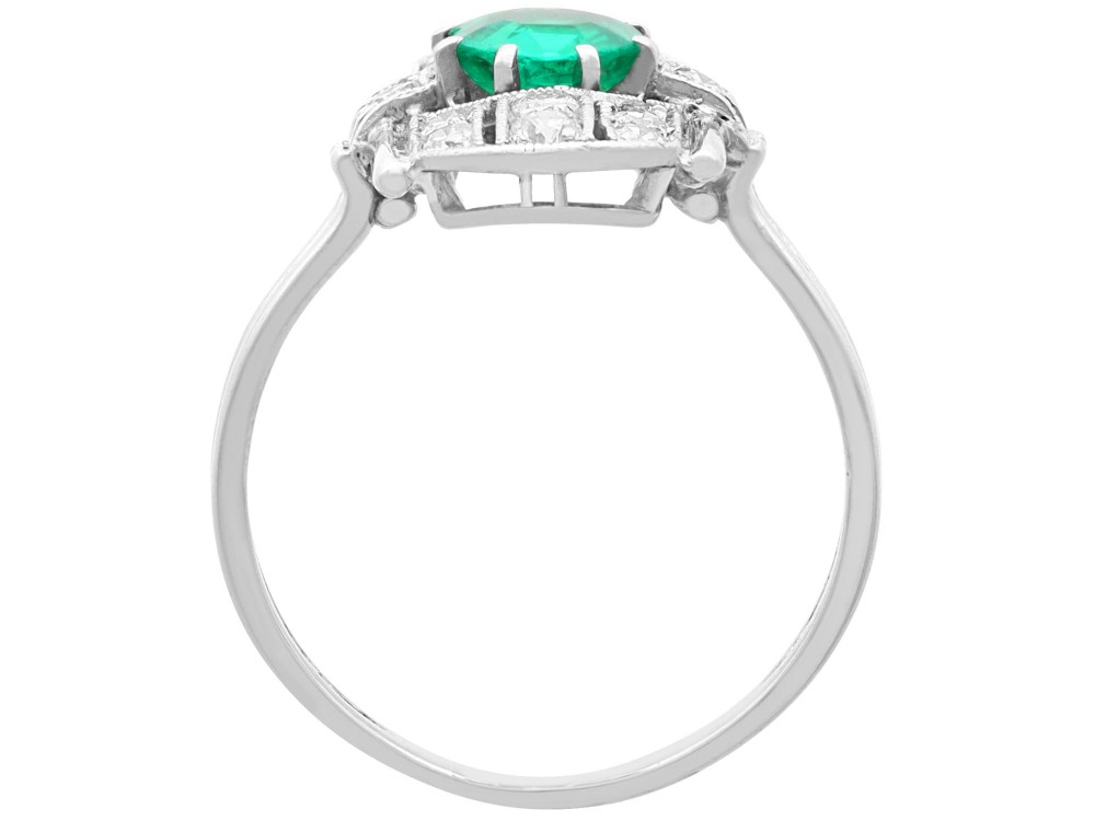 An Art Deco 14ct white gold ring featuring a central round green emerald framed by geometric shoulders set with small brilliant diamonds. View VI