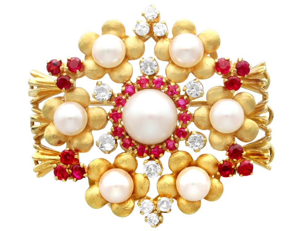 An 18ct yellow gold floral cluster brooch set with a central pearl surrounded by small rubies, outer cultured pearls, round diamonds, and red rubies.