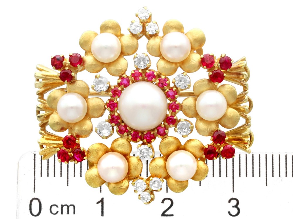 An 18ct yellow gold floral cluster brooch set with a central pearl surrounded by small rubies, outer cultured pearls, round diamonds, and red rubies. View XII