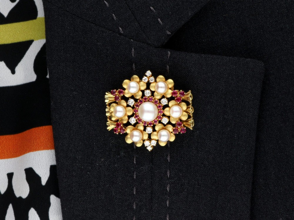 An 18ct yellow gold floral cluster brooch set with a central pearl surrounded by small rubies, outer cultured pearls, round diamonds, and red rubies. View XIV