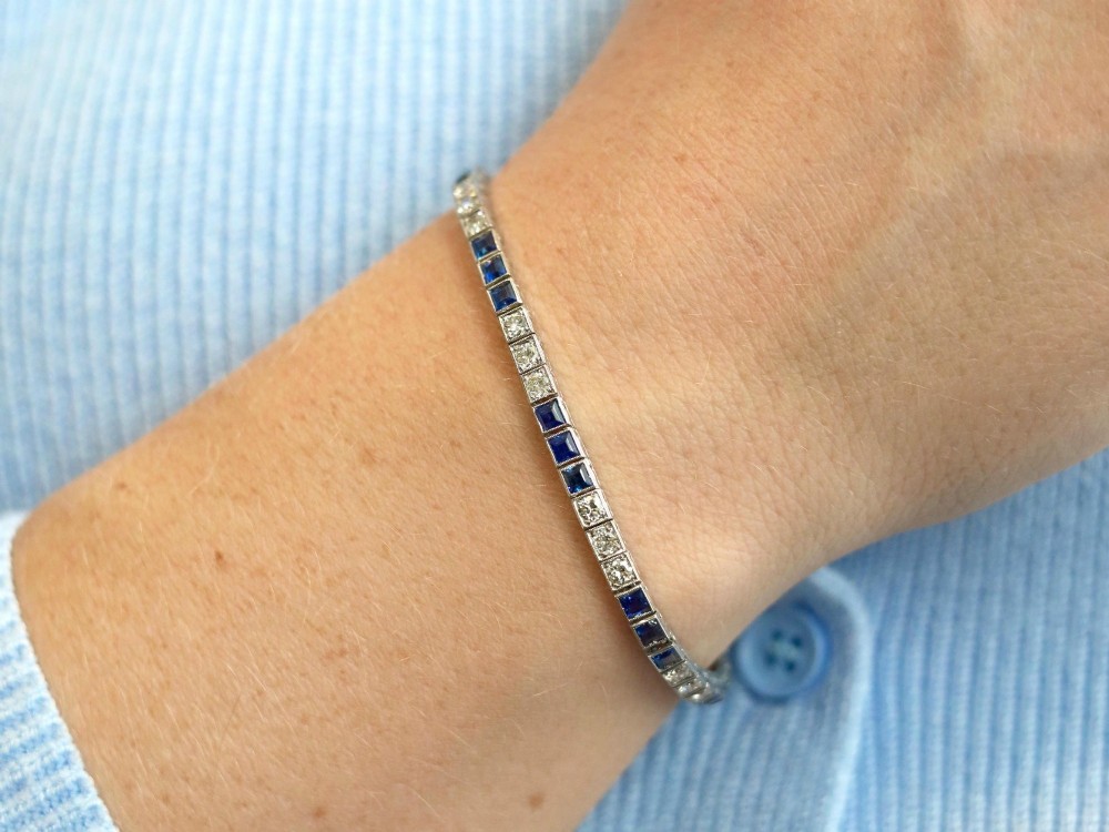 An Art Deco platinum line bracelet set with alternating square blue sapphires and round brilliant diamonds. View IV