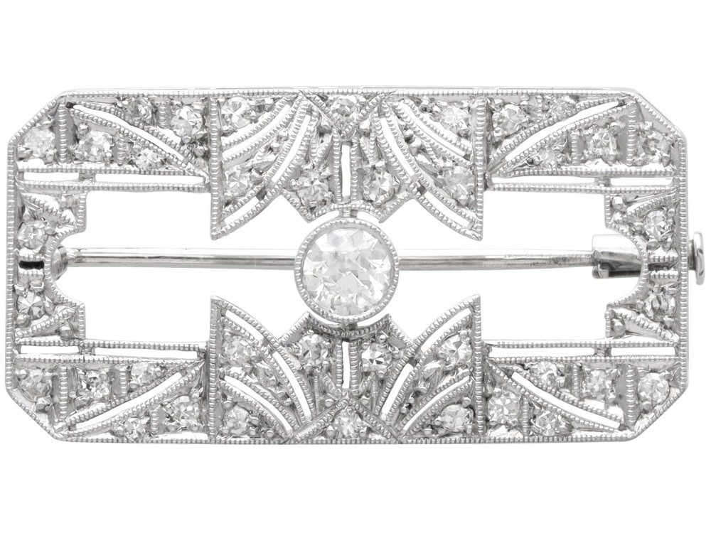 A rectangular Art Deco 18ct white gold brooch featuring openwork geometric filigree, millegrain edging, and a central round-cut diamond.