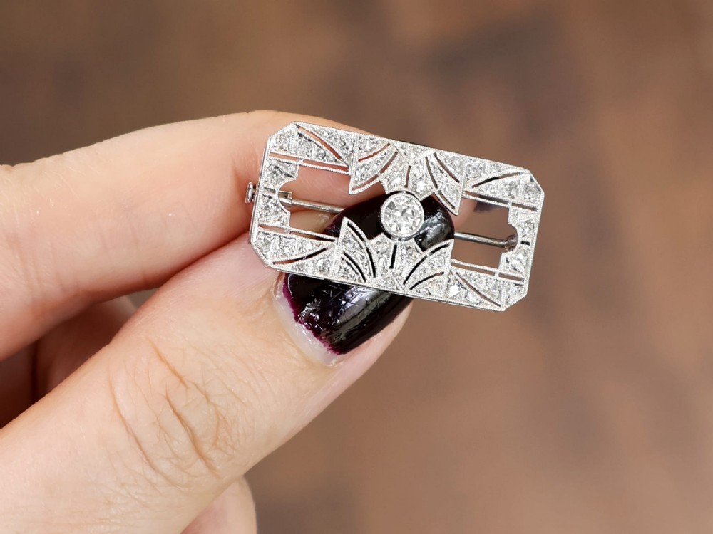 A rectangular Art Deco 18ct white gold brooch featuring openwork geometric filigree, millegrain edging, and a central round-cut diamond. View III