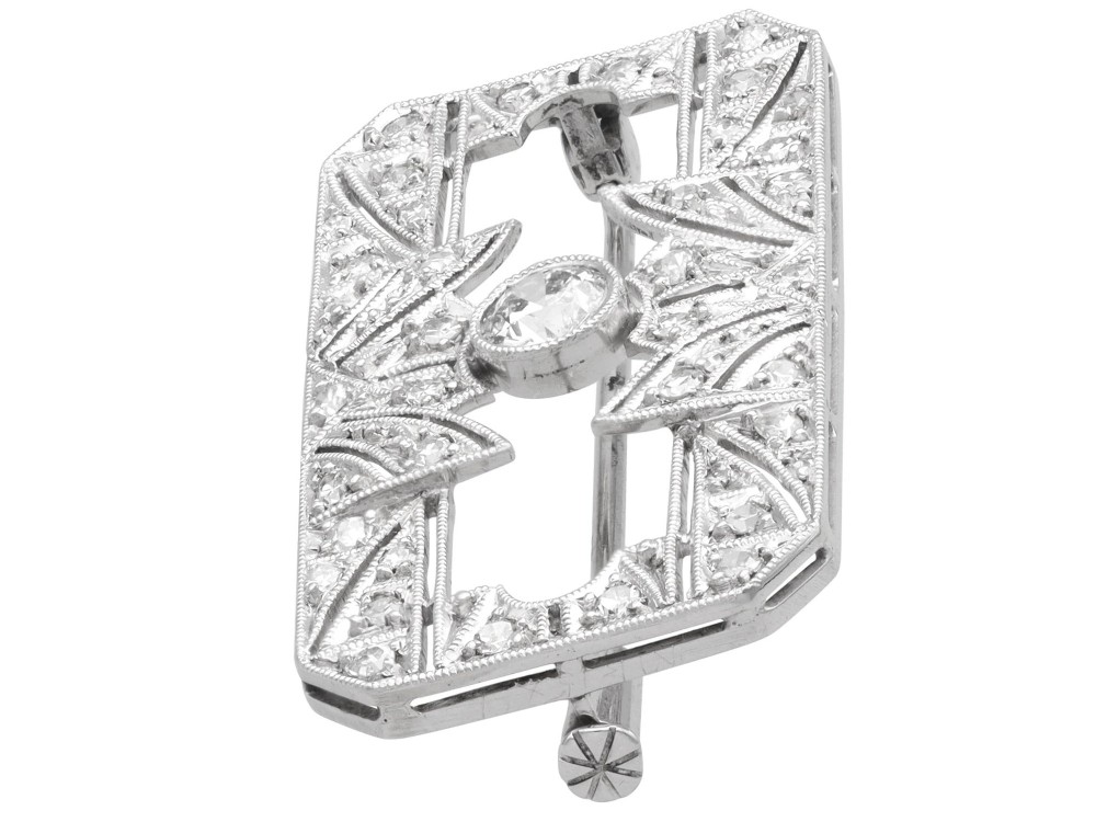 A rectangular Art Deco 18ct white gold brooch featuring openwork geometric filigree, millegrain edging, and a central round-cut diamond. View VII