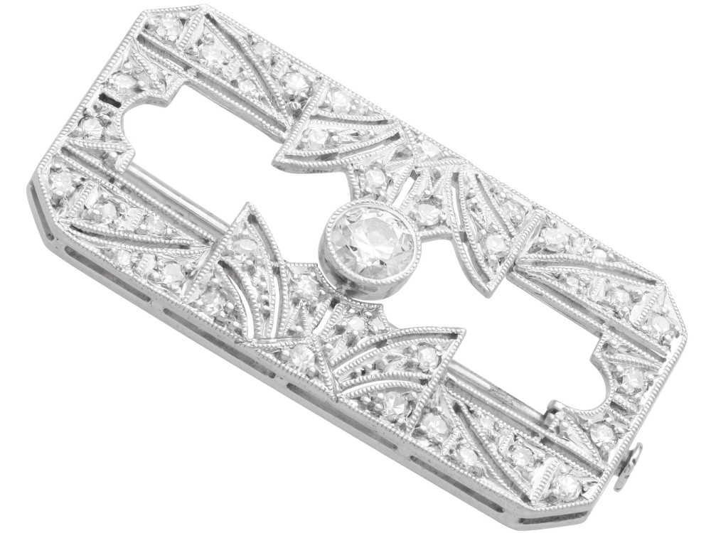 A rectangular Art Deco 18ct white gold brooch featuring openwork geometric filigree, millegrain edging, and a central round-cut diamond. View VIII