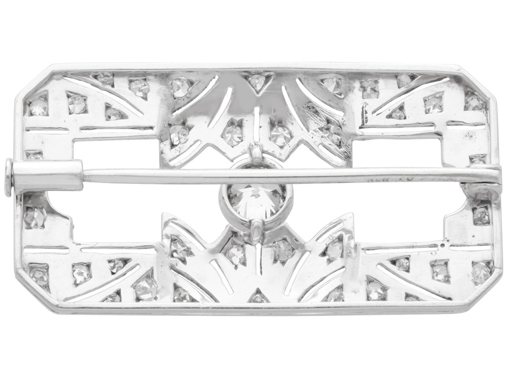 A rectangular Art Deco 18ct white gold brooch featuring openwork geometric filigree, millegrain edging, and a central round-cut diamond. View IX