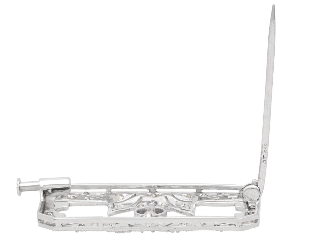 A rectangular Art Deco 18ct white gold brooch featuring openwork geometric filigree, millegrain edging, and a central round-cut diamond. View X