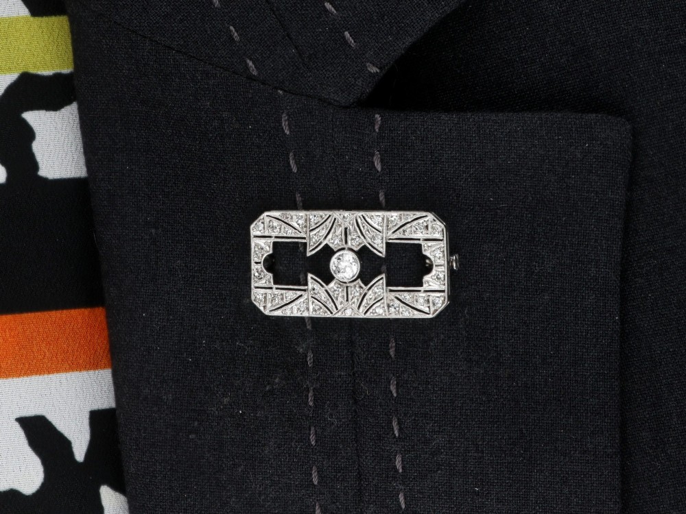 A rectangular Art Deco 18ct white gold brooch featuring openwork geometric filigree, millegrain edging, and a central round-cut diamond. View XII