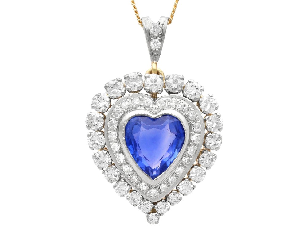 A heart-shaped 14ct yellow gold pendant featuring a central heart-cut Ceylon sapphire surrounded by a double halo of brilliant-cut diamonds.