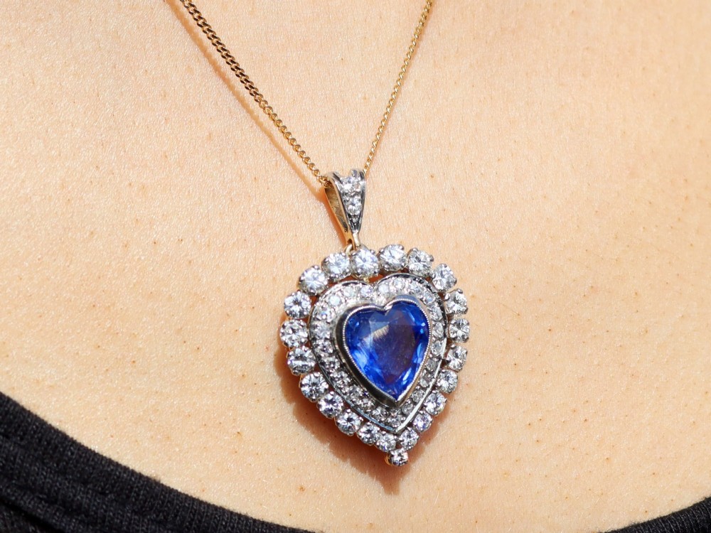 A heart-shaped 14ct yellow gold pendant featuring a central heart-cut Ceylon sapphire surrounded by a double halo of brilliant-cut diamonds. View X