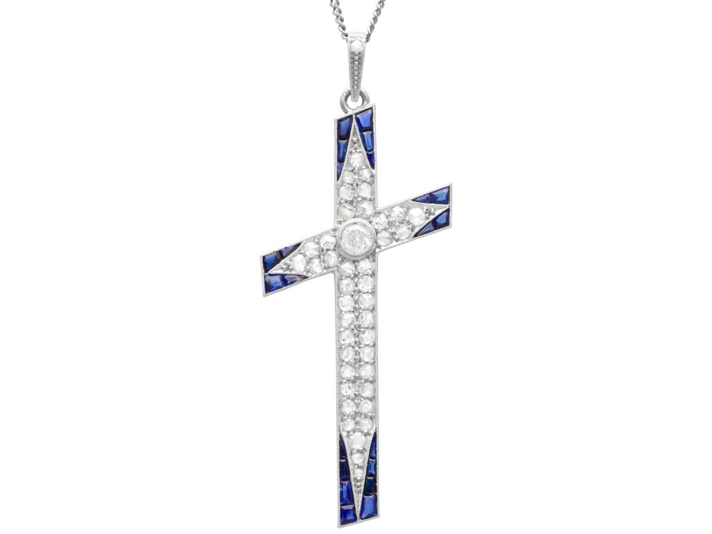 An antique Edwardian cross pendant set with diamonds and geometric blue sapphires suspended from a chain.