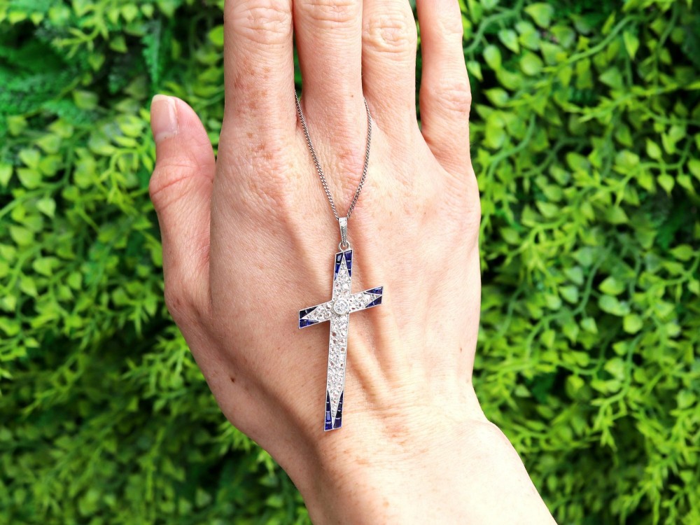 An antique Edwardian cross pendant set with diamonds and geometric blue sapphires suspended from a chain. View II