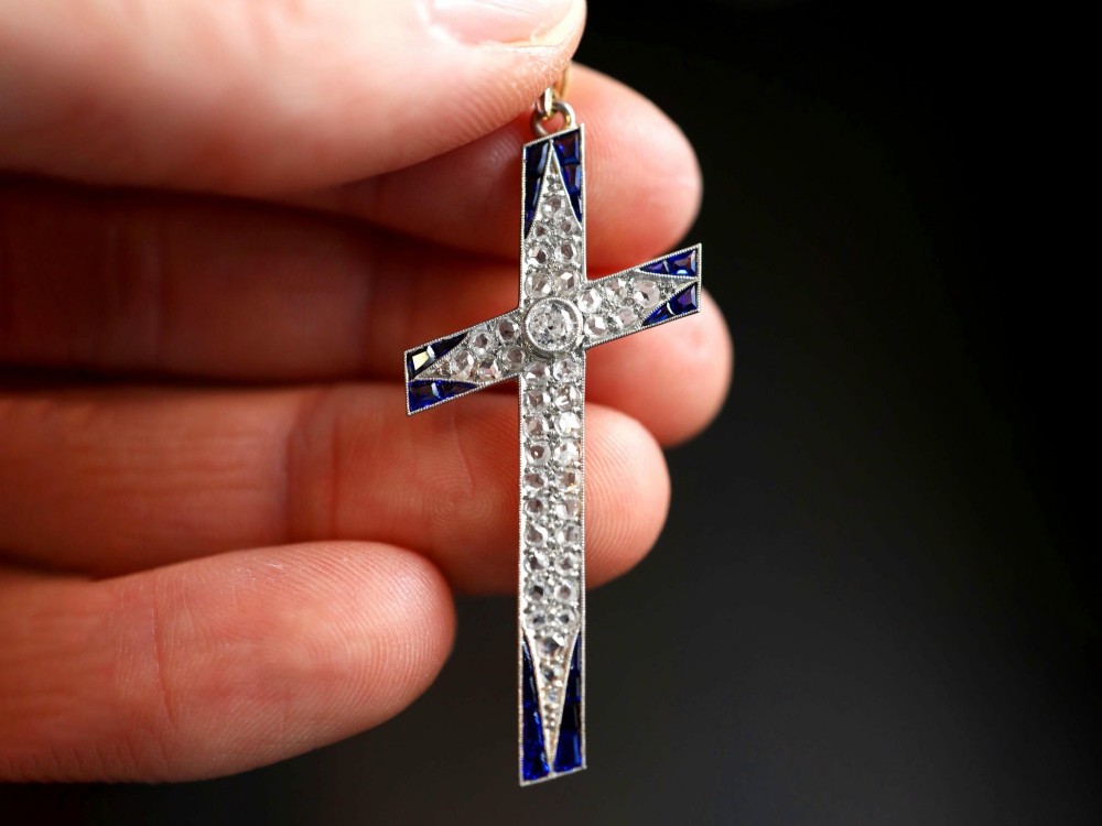 An antique Edwardian cross pendant set with diamonds and geometric blue sapphires suspended from a chain. View III