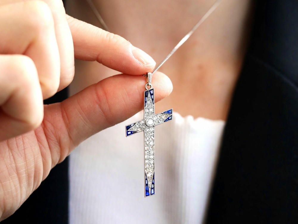 An antique Edwardian cross pendant set with diamonds and geometric blue sapphires suspended from a chain. View V