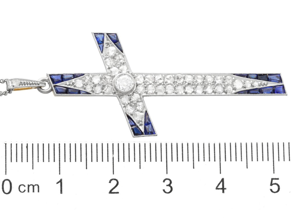 An antique Edwardian cross pendant set with diamonds and geometric blue sapphires suspended from a chain. View IX