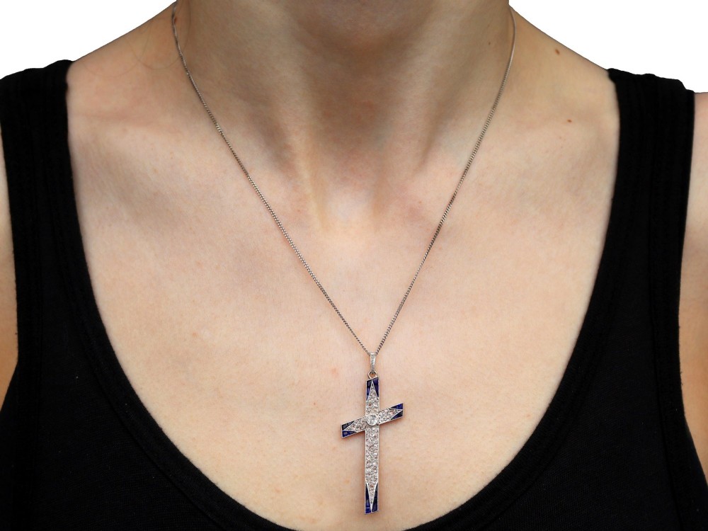 An antique Edwardian cross pendant set with diamonds and geometric blue sapphires suspended from a chain. View X