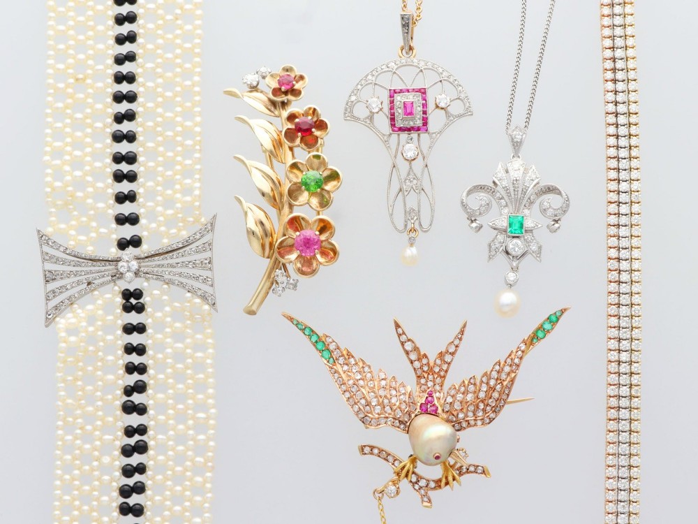 An Art Deco platinum pendant shaped as a stylised fleur-de-lis, embellished with pave-set diamonds, a central rectangular emerald, and a hanging pearl drop. View VI