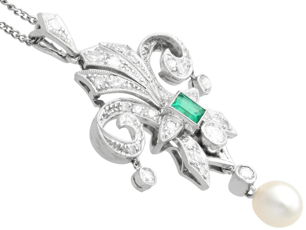 An Art Deco platinum pendant shaped as a stylised fleur-de-lis, embellished with pave-set diamonds, a central rectangular emerald, and a hanging pearl drop. View VIII