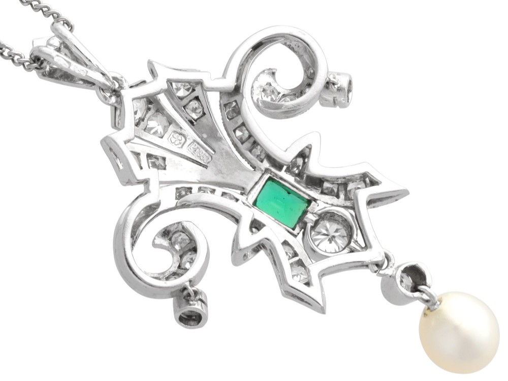 An Art Deco platinum pendant shaped as a stylised fleur-de-lis, embellished with pave-set diamonds, a central rectangular emerald, and a hanging pearl drop. View IX