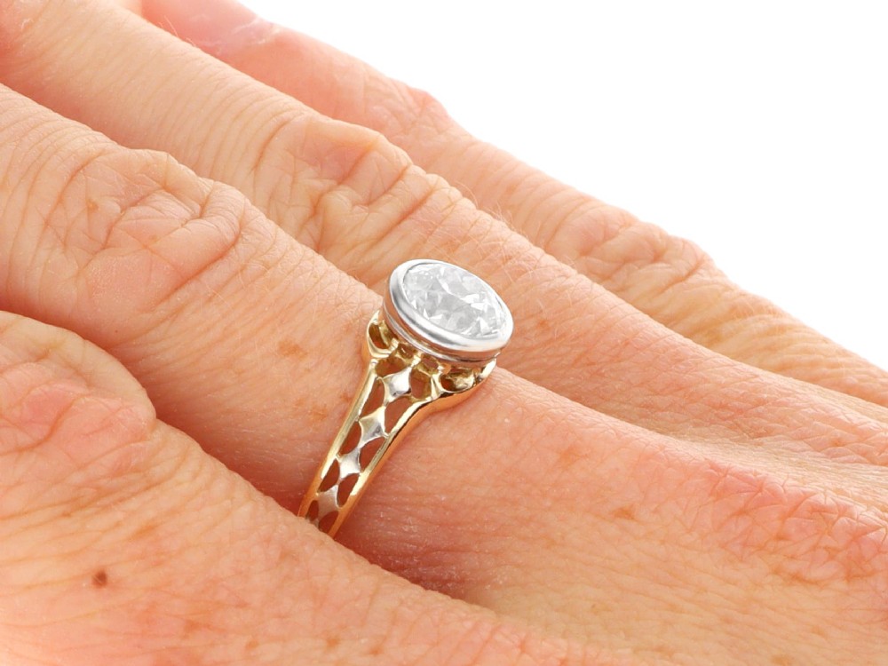 An antique 15ct yellow gold solitaire ring featuring a bezel-set round diamond with decorative openwork shoulders. View X