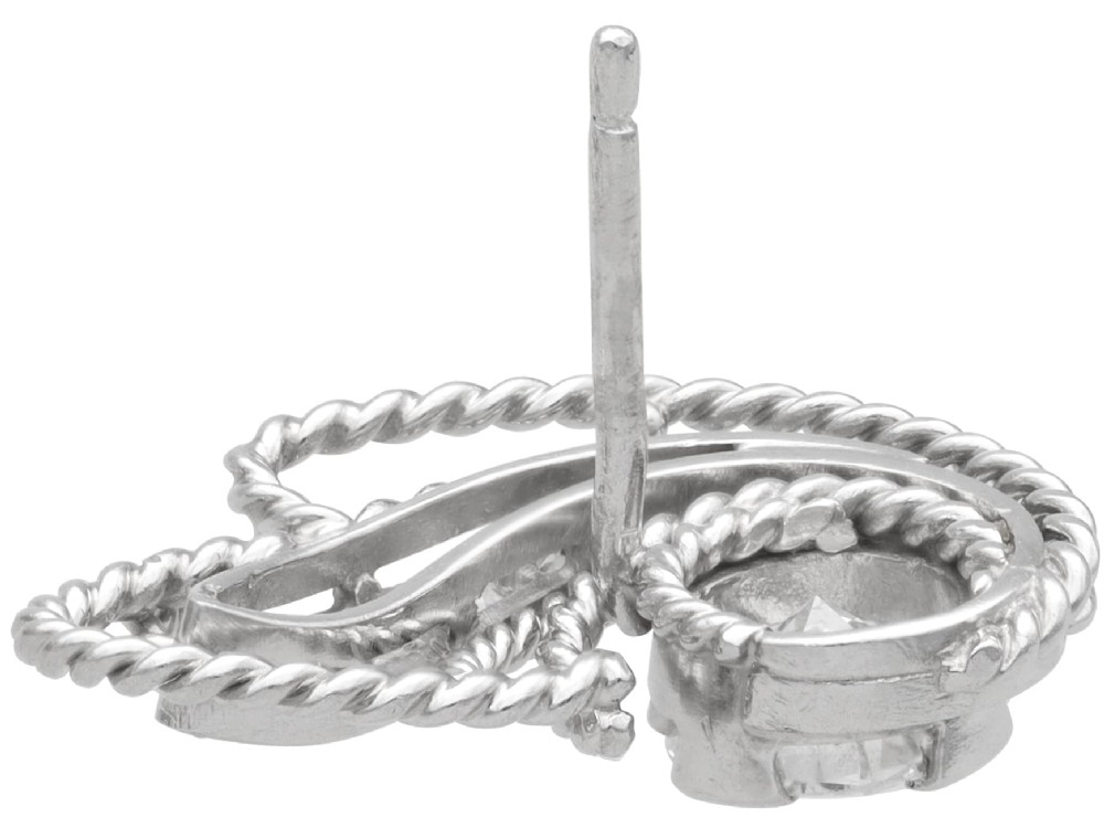 A pair of Art Deco platinum earrings featuring round diamonds set within a textured rope-twist swirl design. View VI