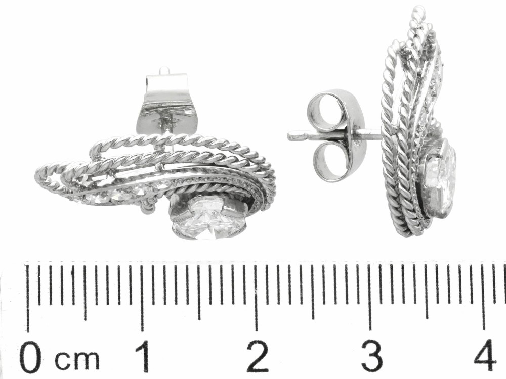 A pair of Art Deco platinum earrings featuring round diamonds set within a textured rope-twist swirl design. View VII