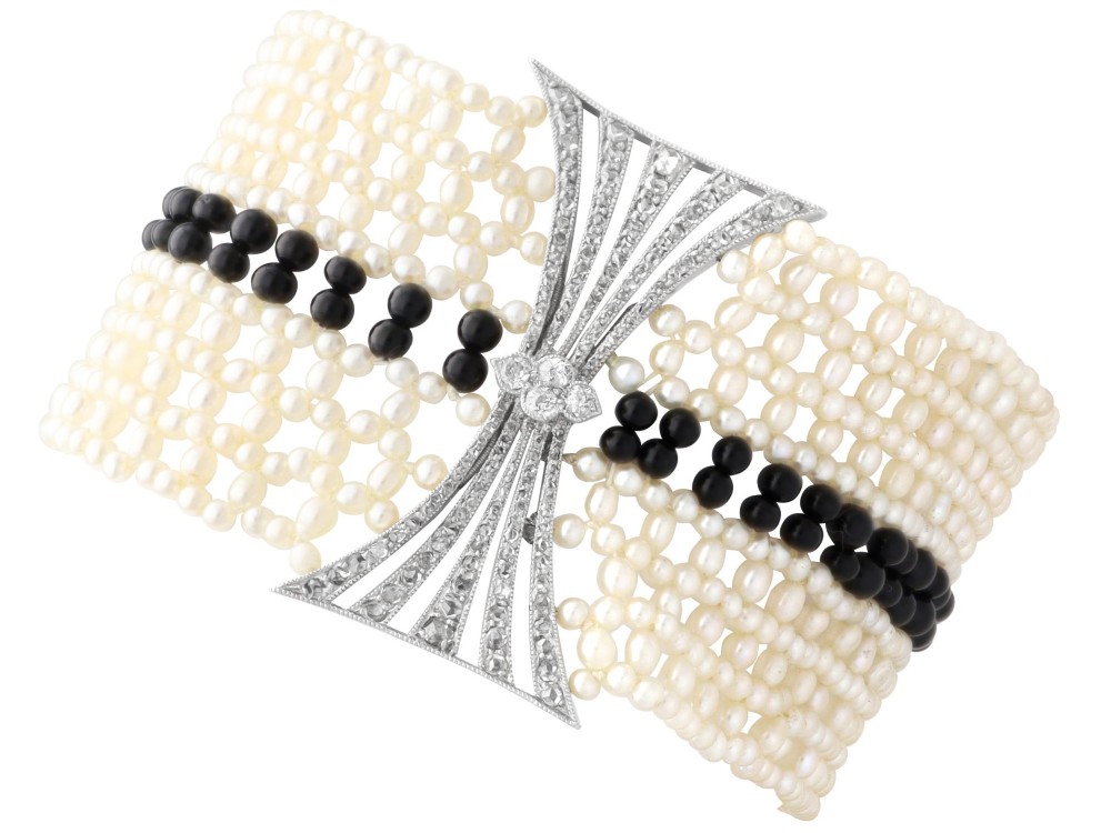 An Art Deco multi-strand pearl and black onyx cuff bracelet featuring a central geometric bow-shaped platinum mount set with diamonds.